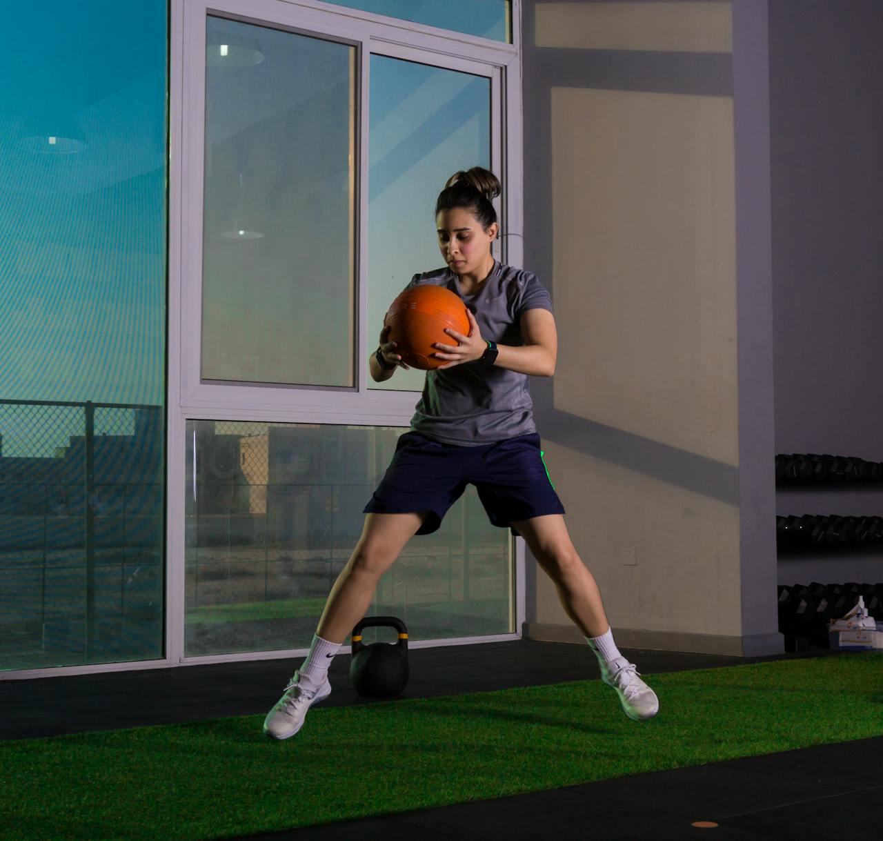 services-02 Focused woman working out indoors using a medicine ball for fitness training.